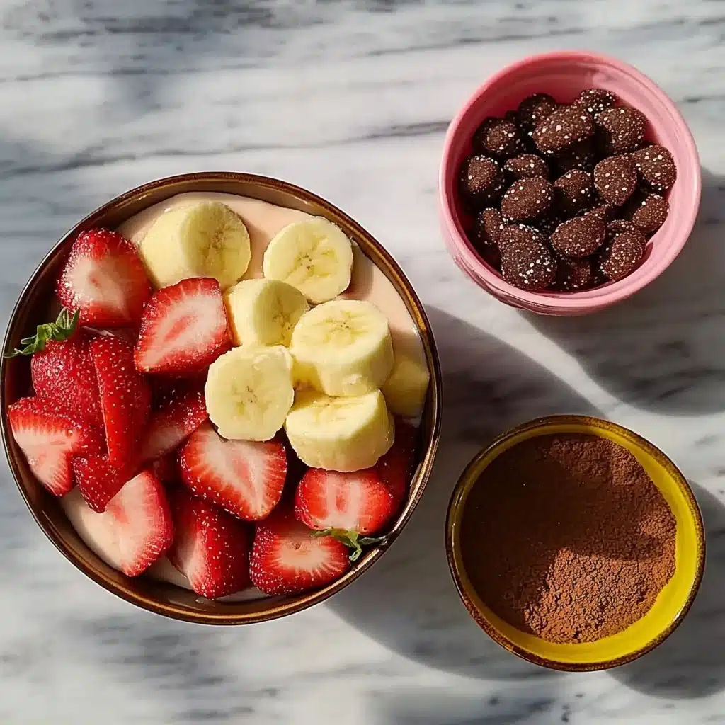 Bananas, strawberries, cocoa powder, and chocolate laid out in bowls